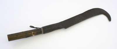 Metal billhook with wooden handle, undated. The billhook is a traditional agriculture tool used for cutting shrubs and branches and it was once made by the local blacksmith. There are many types and the shape depends on which part of the UK it comes from.