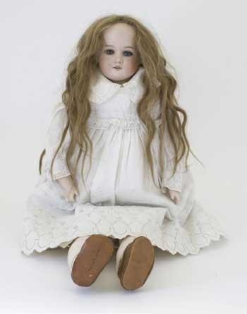 Doll with ceramic face arms and legs, and long blonde hair, circa 1910. She is about 64cm tall and is dressed in a white broiderie Anglais dress, cotton socks and brown leather shoes. Probably made from bisque, the fashionable material for dolls.