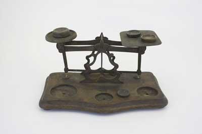 Victorian brass postal scales with a circular plate for the weights and a square plate for the letters with details of current postage rates. Circular depressions to hold the weights can be seen on the base. 