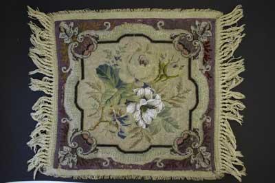 Victorian beadwork and embroidery sampler. The design of the sampler depicts flowers in the centre and is surrounded by a border and fringing on two sides. The colours are much faded (shown by brighter colour of thread at the back of piece).