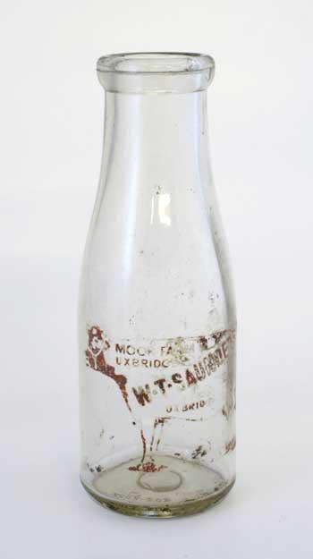 Large milk bottle with wide neck and top. Printed inside the outline of a cow is Moor Farm Uxbridge - W T Saunders - milk direct from the farm.
