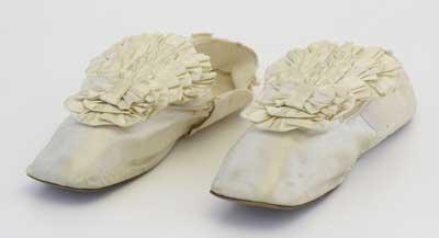 Early Victorian white satin shoes with kid lining and decorated with satin rosettes. They were worn at the wedding of the donor's mother, Fanny Caroline Webster on April 14, 1877.